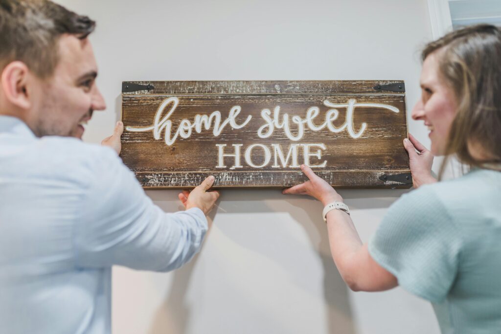A couple happily mounts a 'Home Sweet Home' sign in their new house.